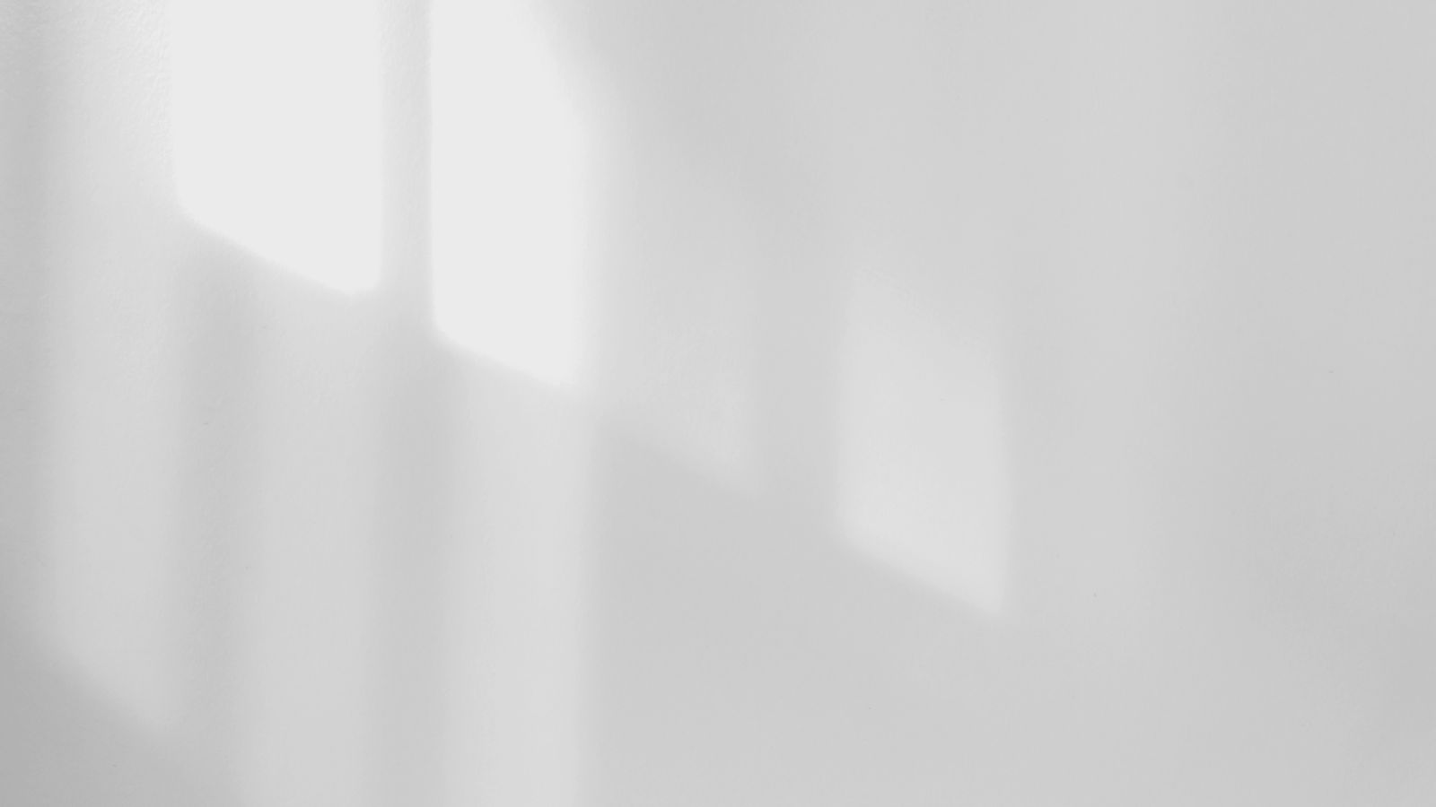 A bare white wall with the soft diagonal shadow of a window falling across it