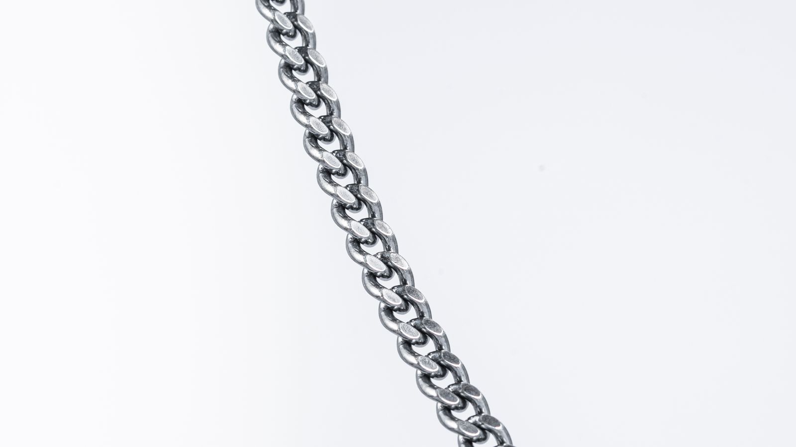 A fine silver chain lying in a diagonal line across a plain white surface